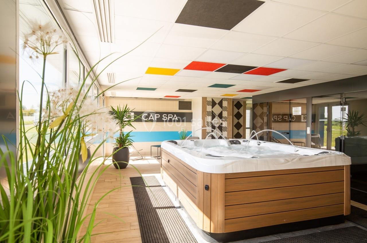 Bain à remous dans une pièce lumineuse avec des plantes, un sol en bois et un plafond décoré de panneaux colorés.