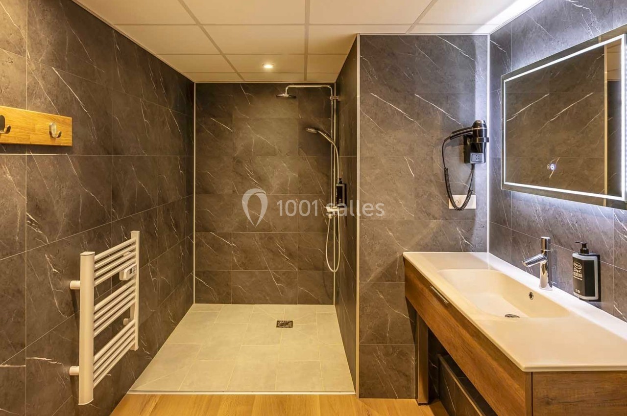 Salle de bain moderne avec douche à l'italienne, carrelage gris foncé, lavabo en bois et miroir éclairé.