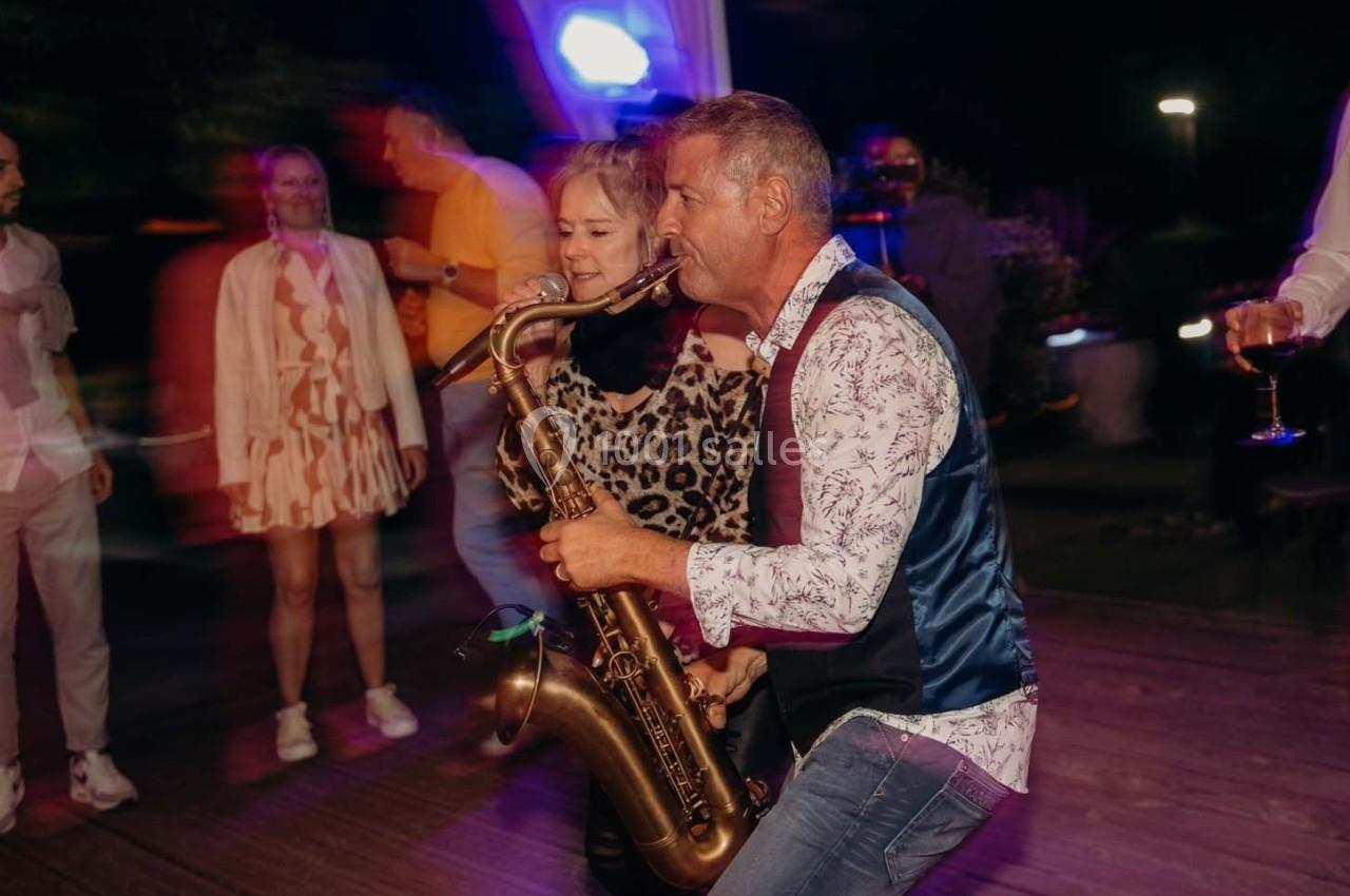 Un musicien joue du saxophone sur une scène, accompagné d'une chanteuse, devant un public en mouvement.