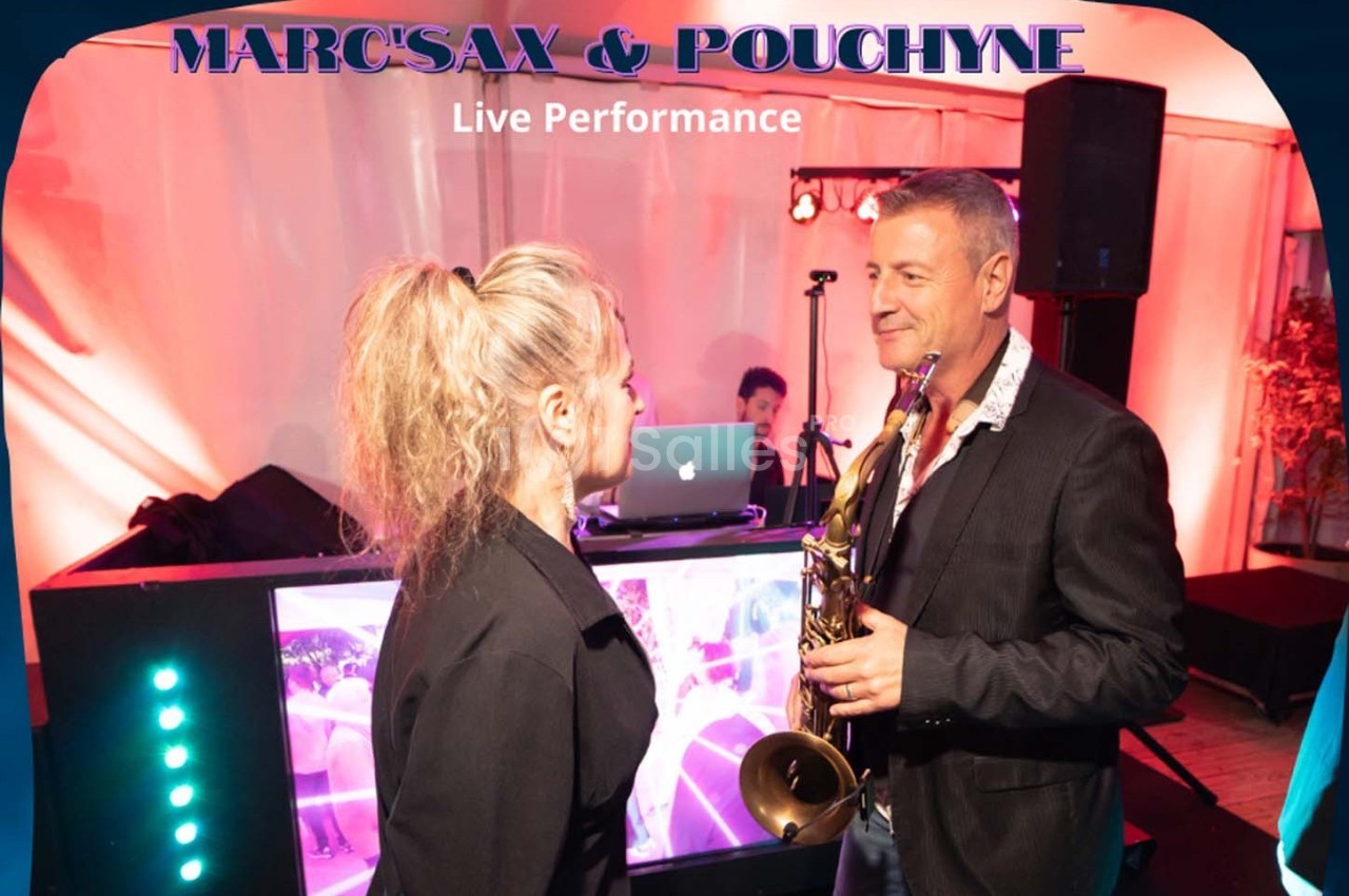 Un musicien tenant un saxophone échange avec une femme devant une scène éclairée lors d'une performance en direct.