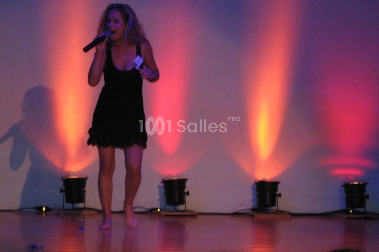 Une femme chante pieds nus sur une scène éclairée par des projecteurs aux teintes orange et violette.
