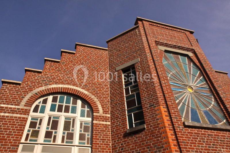 Façade en briques rouges avec des fenêtres en vitraux colorés et un motif en éventail sous un ciel bleu.