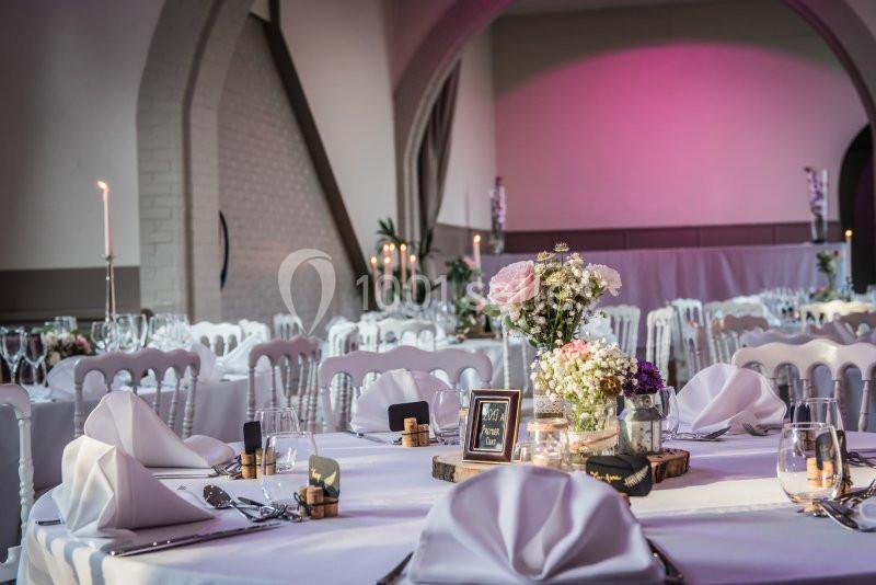 Salle de réception décorée avec des tables élégantes, nappes blanches, bougies et arrangements floraux.