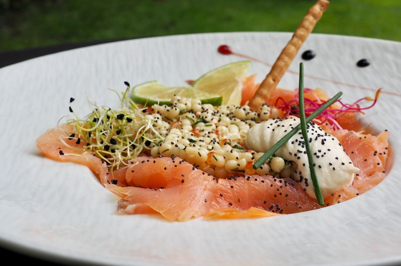 Assiette de saumon fumé avec graines, germes, crème fraîche, citron vert et décorations culinaires.