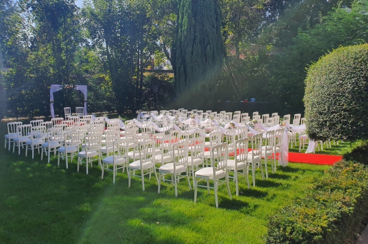 Chaises blanches alignées en extérieur pour une cérémonie, entourées de verdure et éclairées par le soleil.