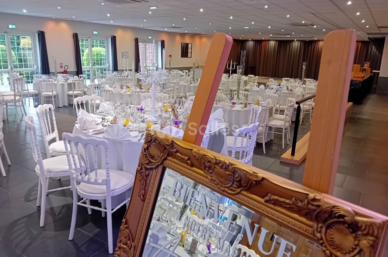 Salle de réception élégamment décorée avec des tables rondes dressées et un miroir doré au premier plan.