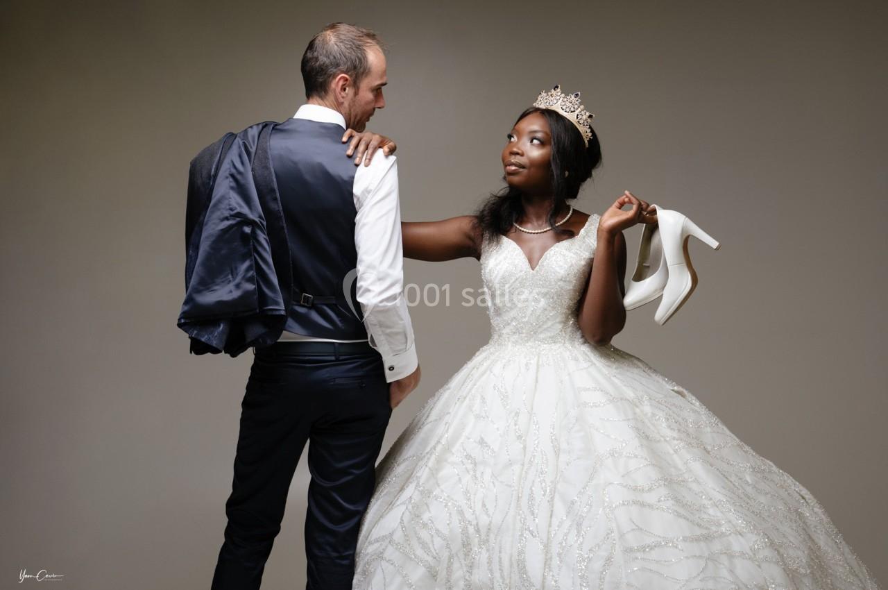 Un couple en tenue de mariage, la mariée tenant ses chaussures blanches et regardant le marié.