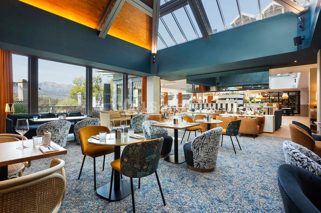 Salle de restaurant lumineuse avec de grandes baies vitrées, mobilier varié et décoration moderne.