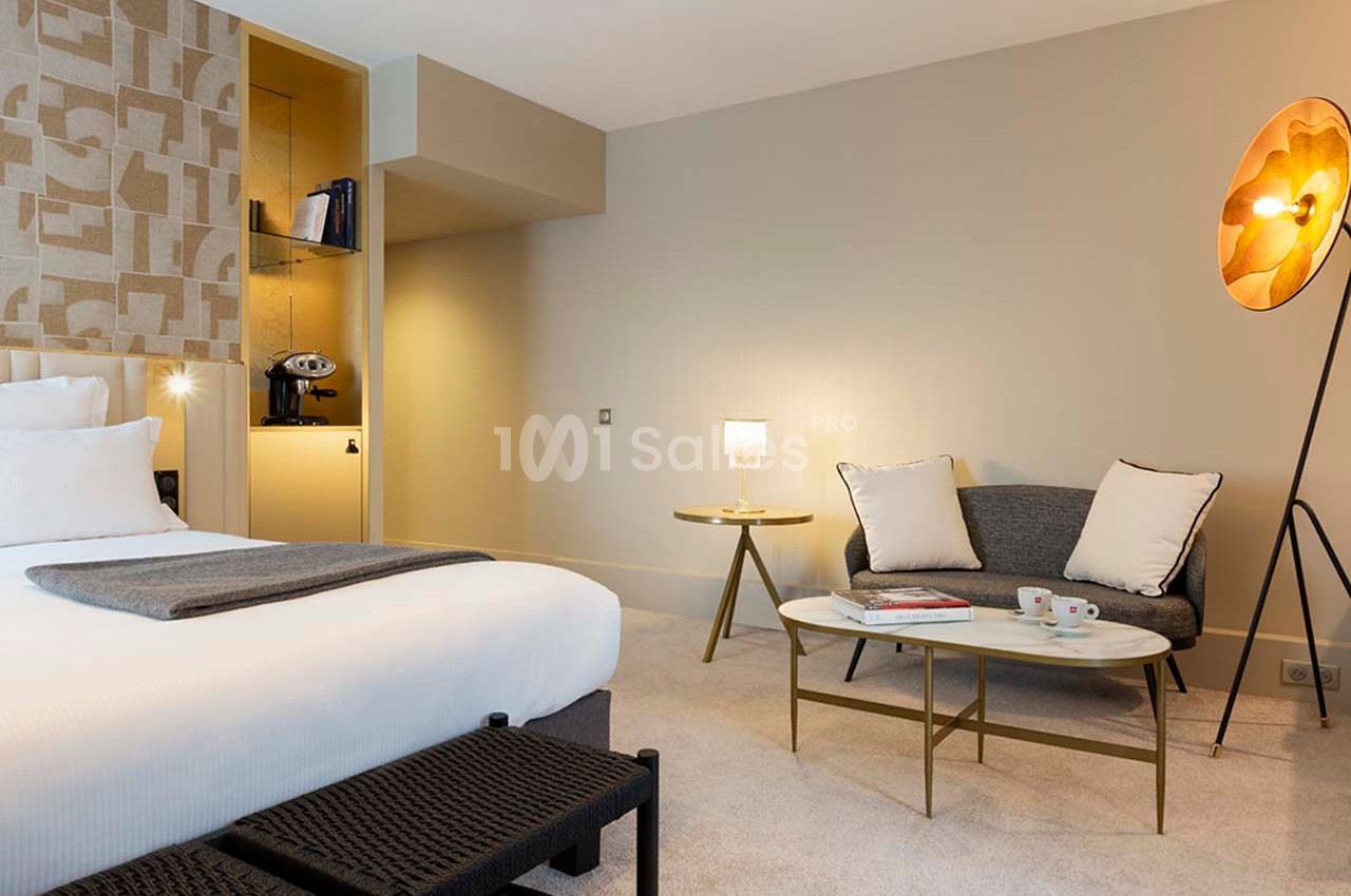 Chambre lumineuse avec lit double, canapé, table basse, lampes modernes et décoration murale géométrique.