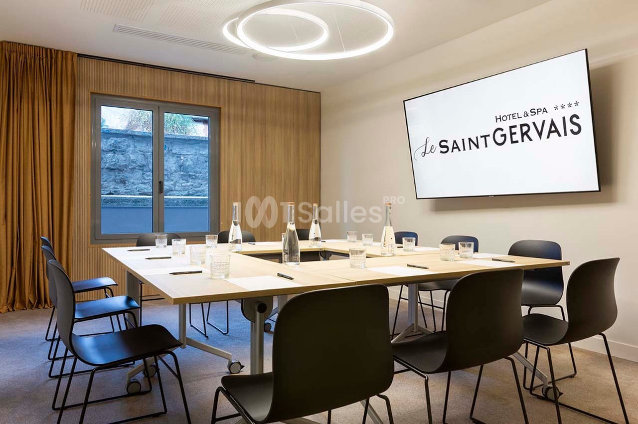 Salle de réunion moderne avec table rectangulaire, chaises noires, écran mural et bouteilles d'eau disposées.
