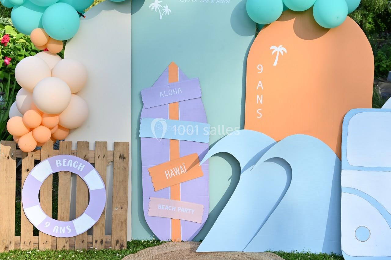 Décor festif sur le thème de la plage avec planche de surf, bouée, vagues et ballons colorés.