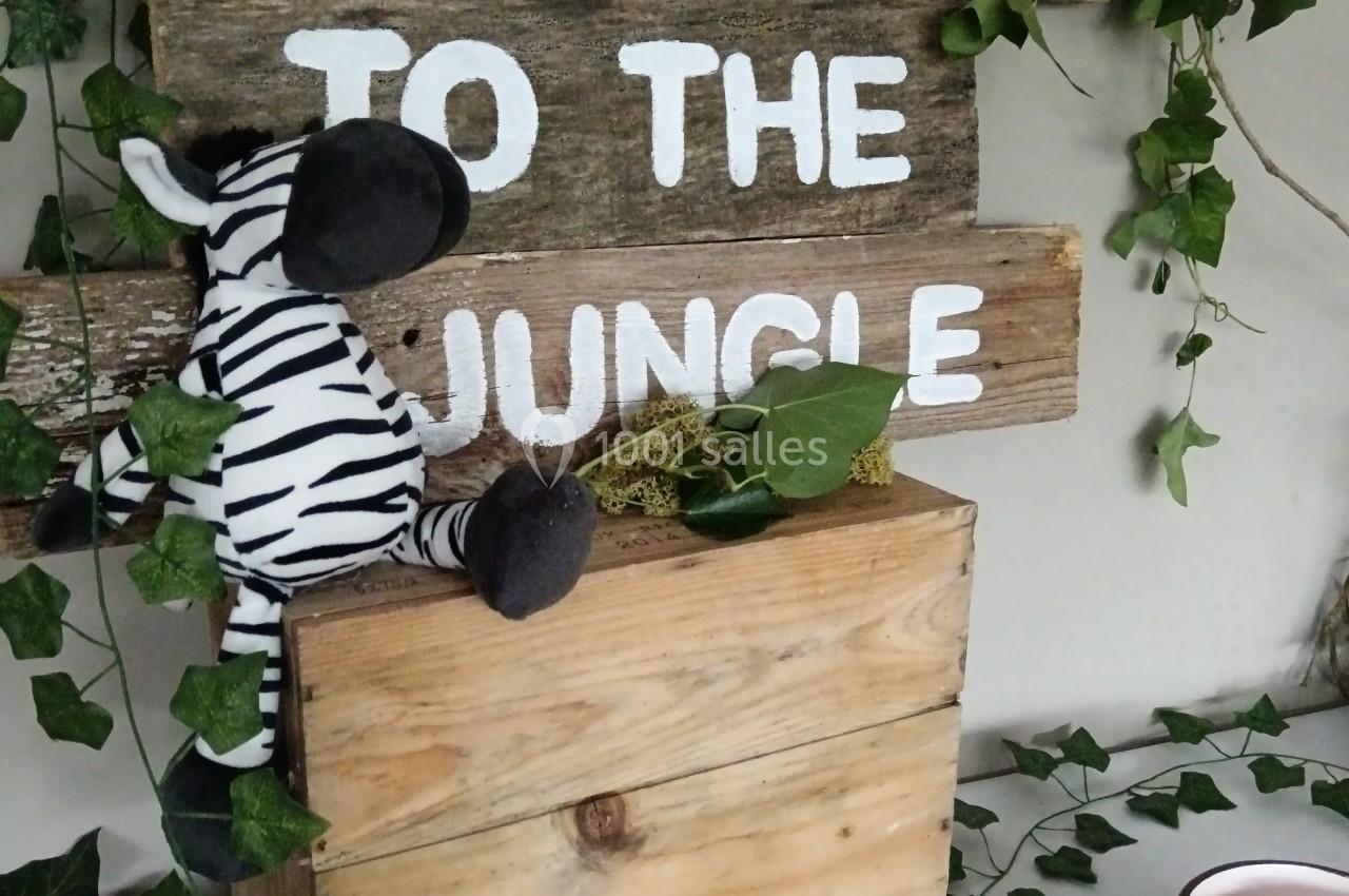 Panneau en bois ’Welcome to the Jungle’ décoré de lierre, avec une peluche zèbre et des éléments tropicaux.