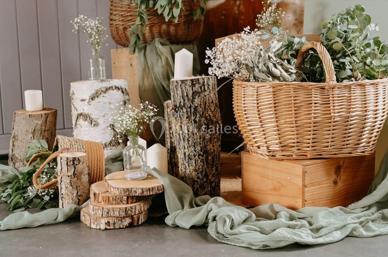 Décoration rustique avec rondins de bois, bougies, panier en osier et feuillages sur un sol en tissu vert.