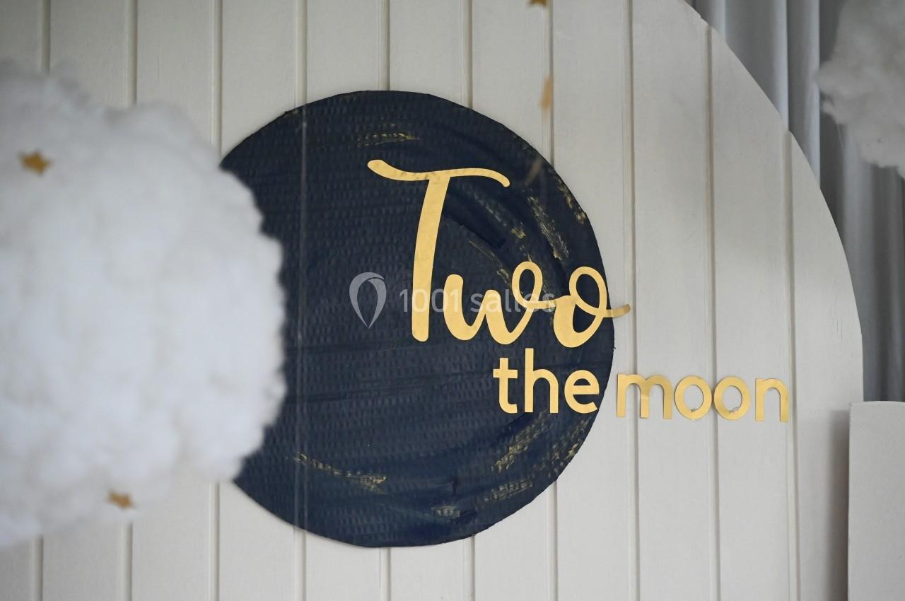 Panneau décoratif avec l'inscription ’Two the moon’ en lettres dorées sur un fond circulaire noir, entouré de nuages.