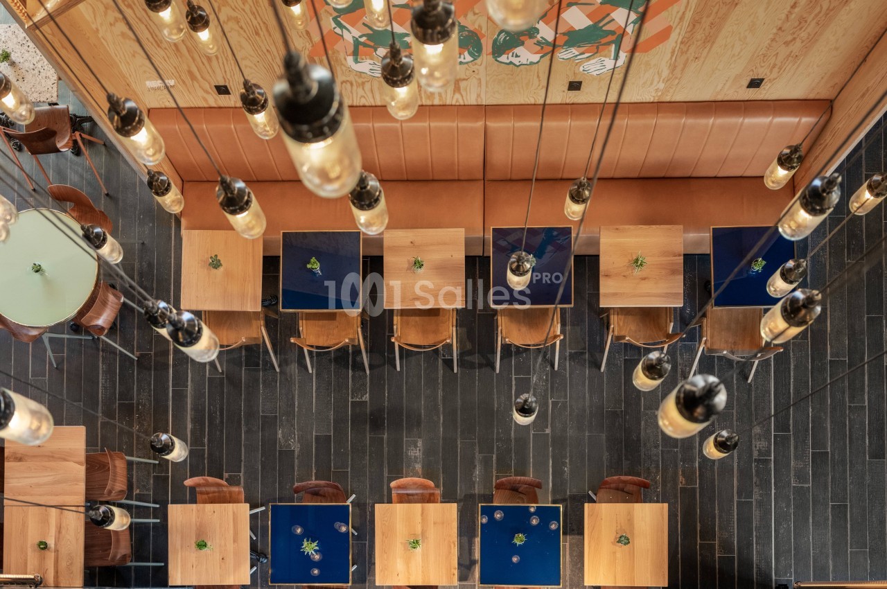 Vue plongeante sur une salle de restaurant avec des tables en bois, des chaises et un éclairage suspendu.