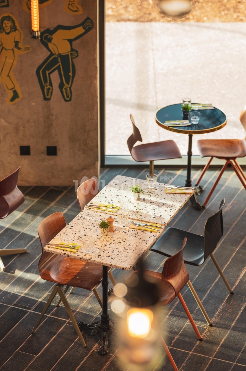 Salle de restaurant moderne avec tables dressées, chaises en bois et décoration murale artistique.