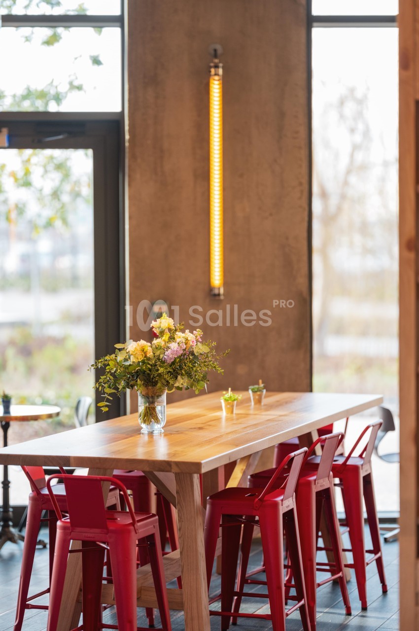 Table en bois entourée de chaises rouges, décorée avec un vase de fleurs, dans un intérieur lumineux et moderne.