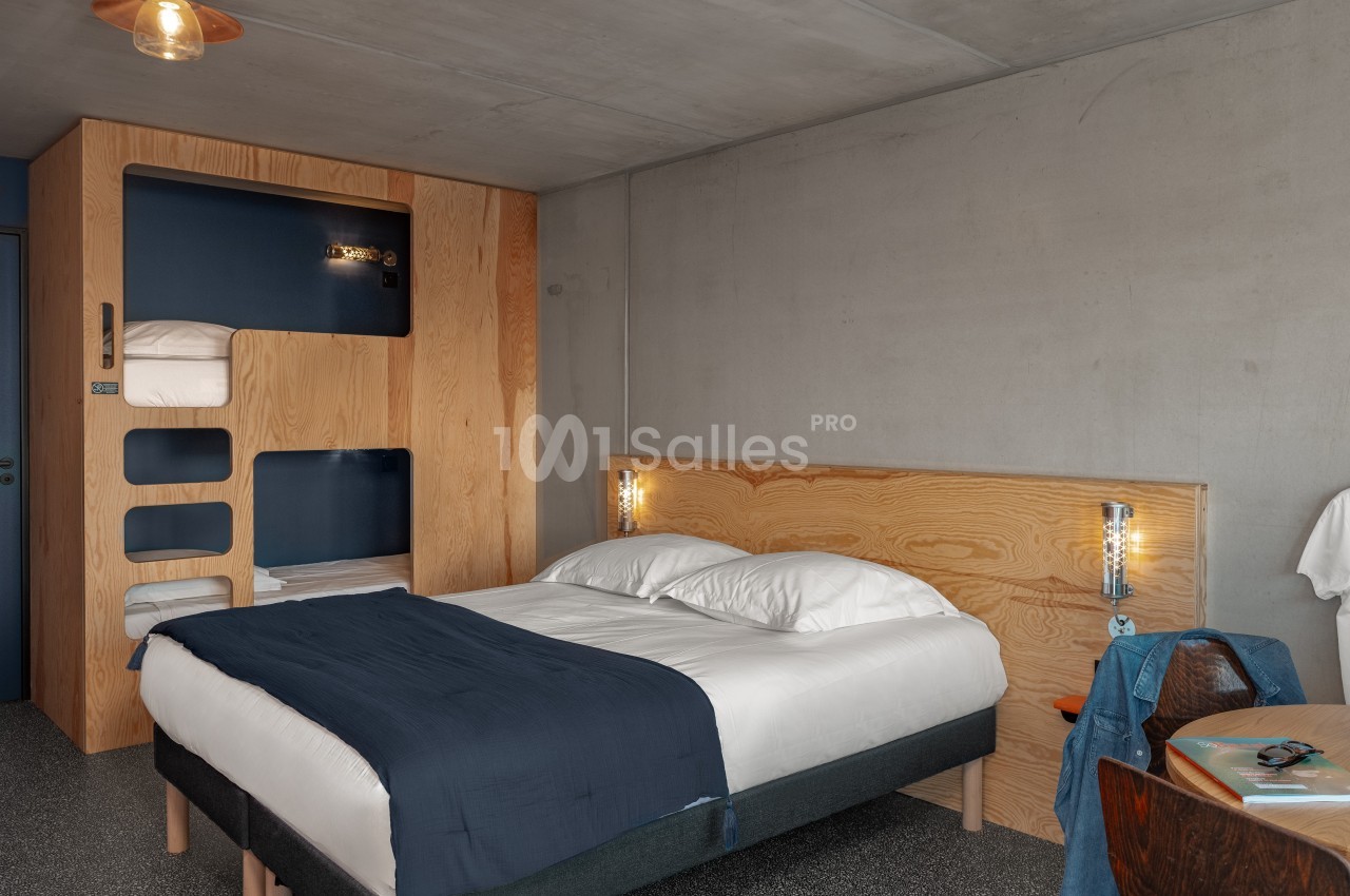 Chambre moderne avec lit double, literie blanche et bleue, mobilier en bois clair et éclairage minimaliste.
