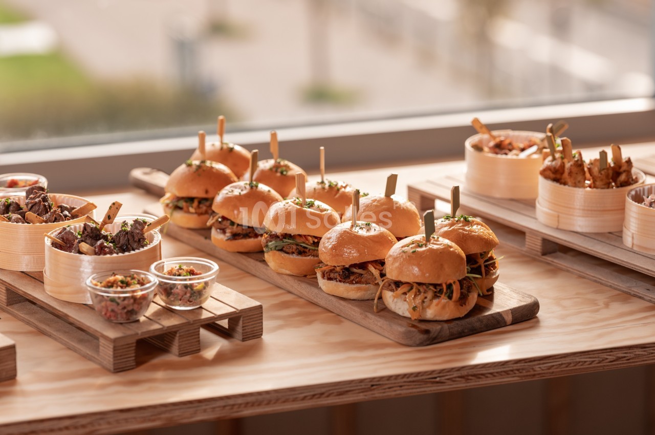 Plateau en bois avec burgers garnis, accompagnés de salades et de petites portions dans des bols en bambou.