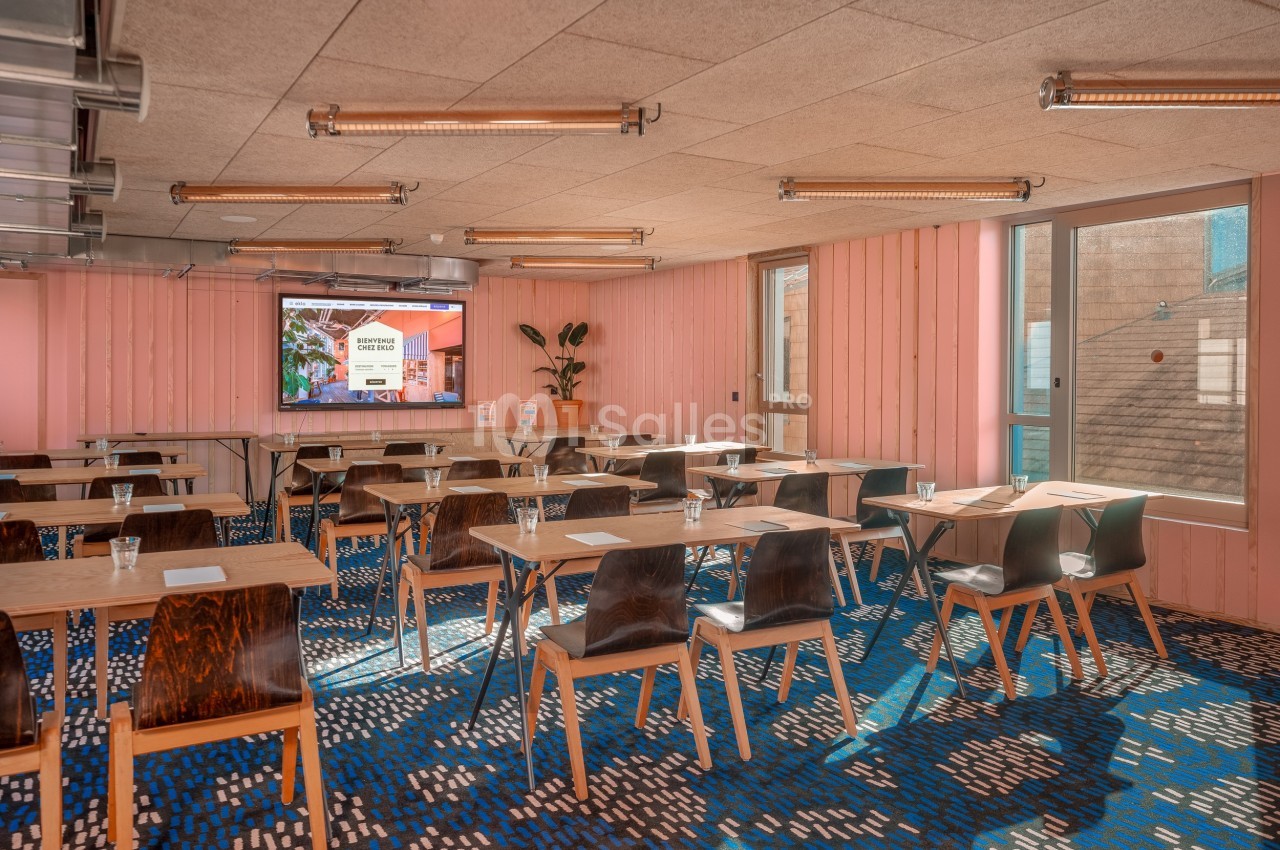 Salle de réunion lumineuse avec des tables en bois, des chaises modernes et un écran de présentation au fond.