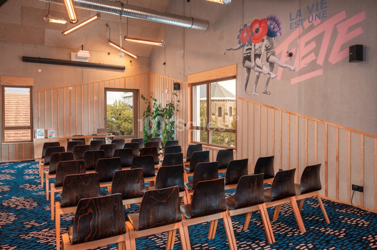 Salle de réunion avec des rangées de chaises en bois, décor moderne et mur avec une fresque colorée.