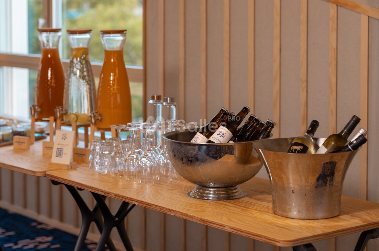 Buffet avec carafes de jus, verres, bouteilles de bière et de vin disposés sur une table en bois.