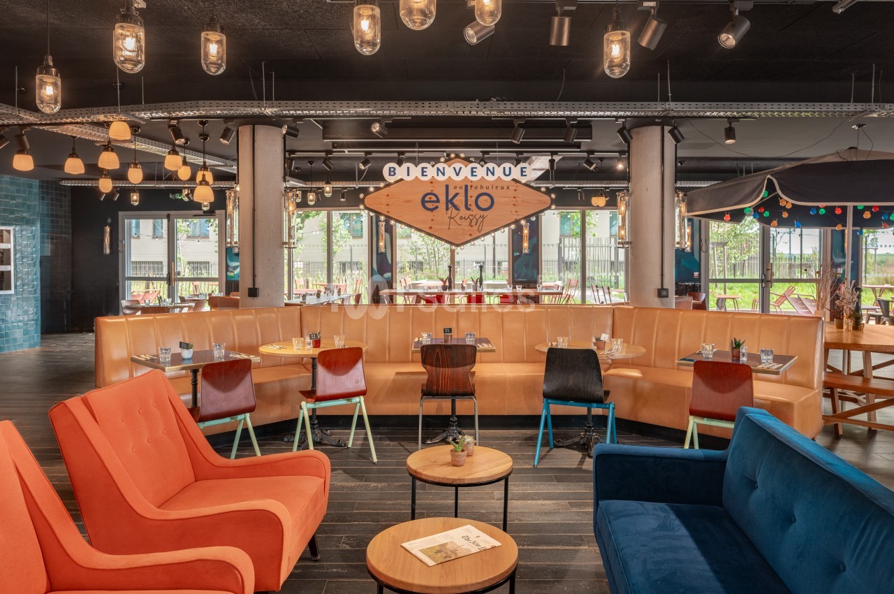 Espace lounge lumineux avec canapés colorés, tables dressées et panneau ’Bienvenue Eklo’ en arrière-plan.