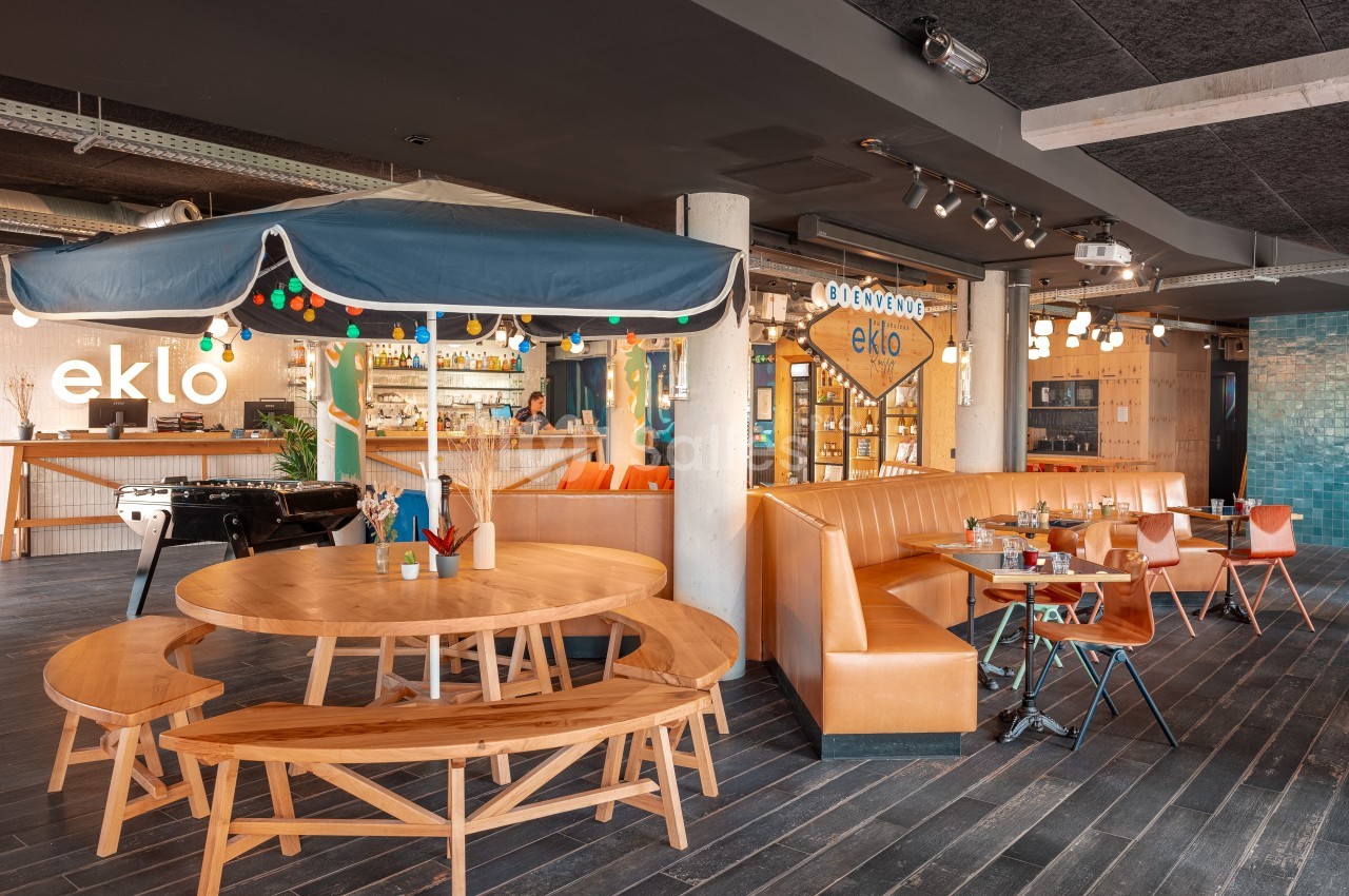 Espace de restauration moderne avec tables en bois, banquettes orange, éclairage chaleureux et décoration colorée.
