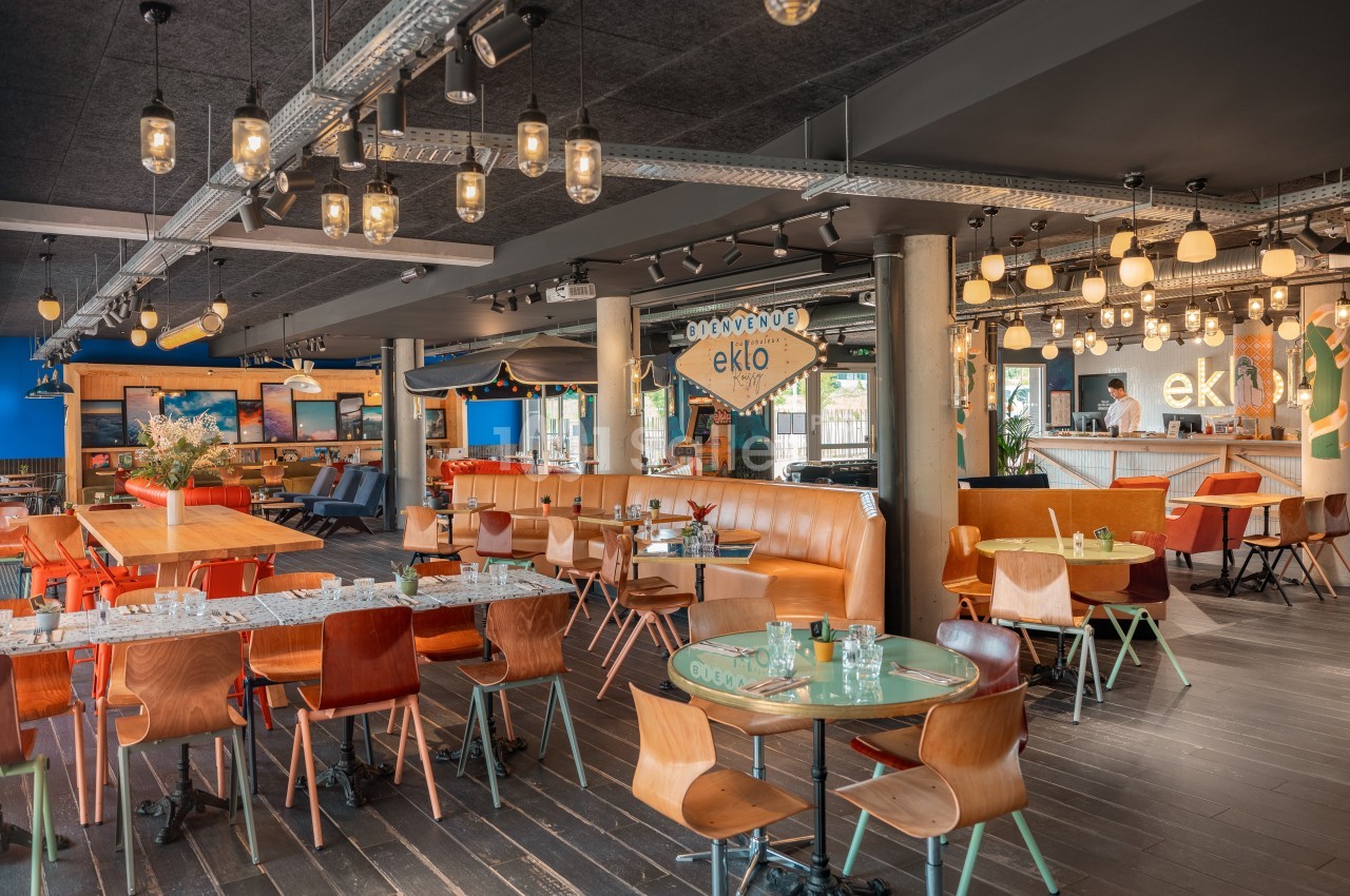 Salle de restaurant moderne avec tables en bois, banquettes orange et éclairage suspendu.