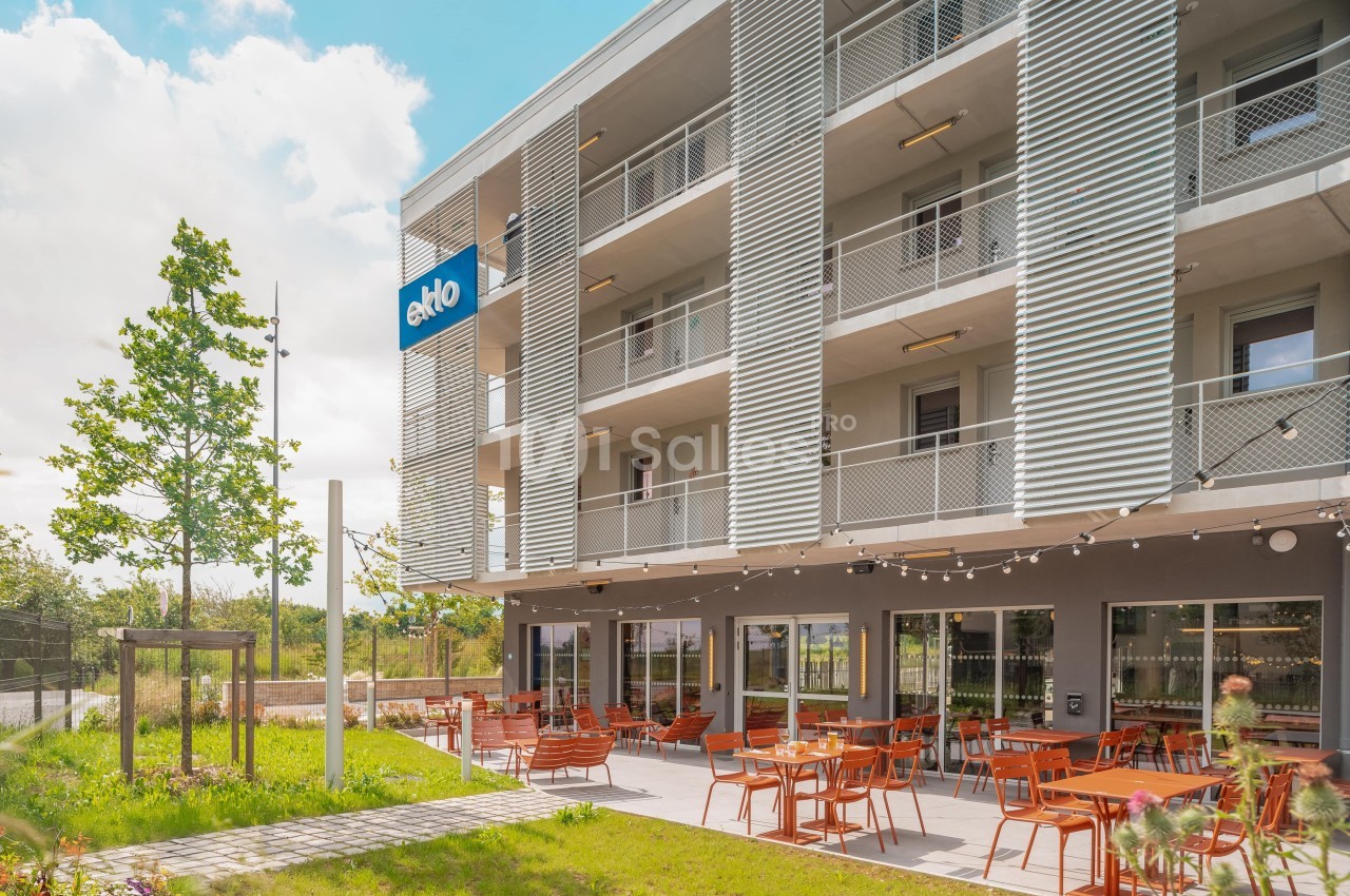 Façade d'un bâtiment moderne avec balcons, terrasse aménagée et enseigne ’Eklo’, entouré de verdure.