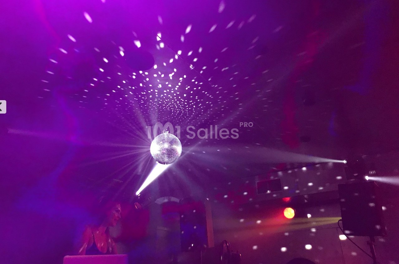 Une boule à facettes illumine une salle sombre avec des reflets lumineux, créant une ambiance festive.