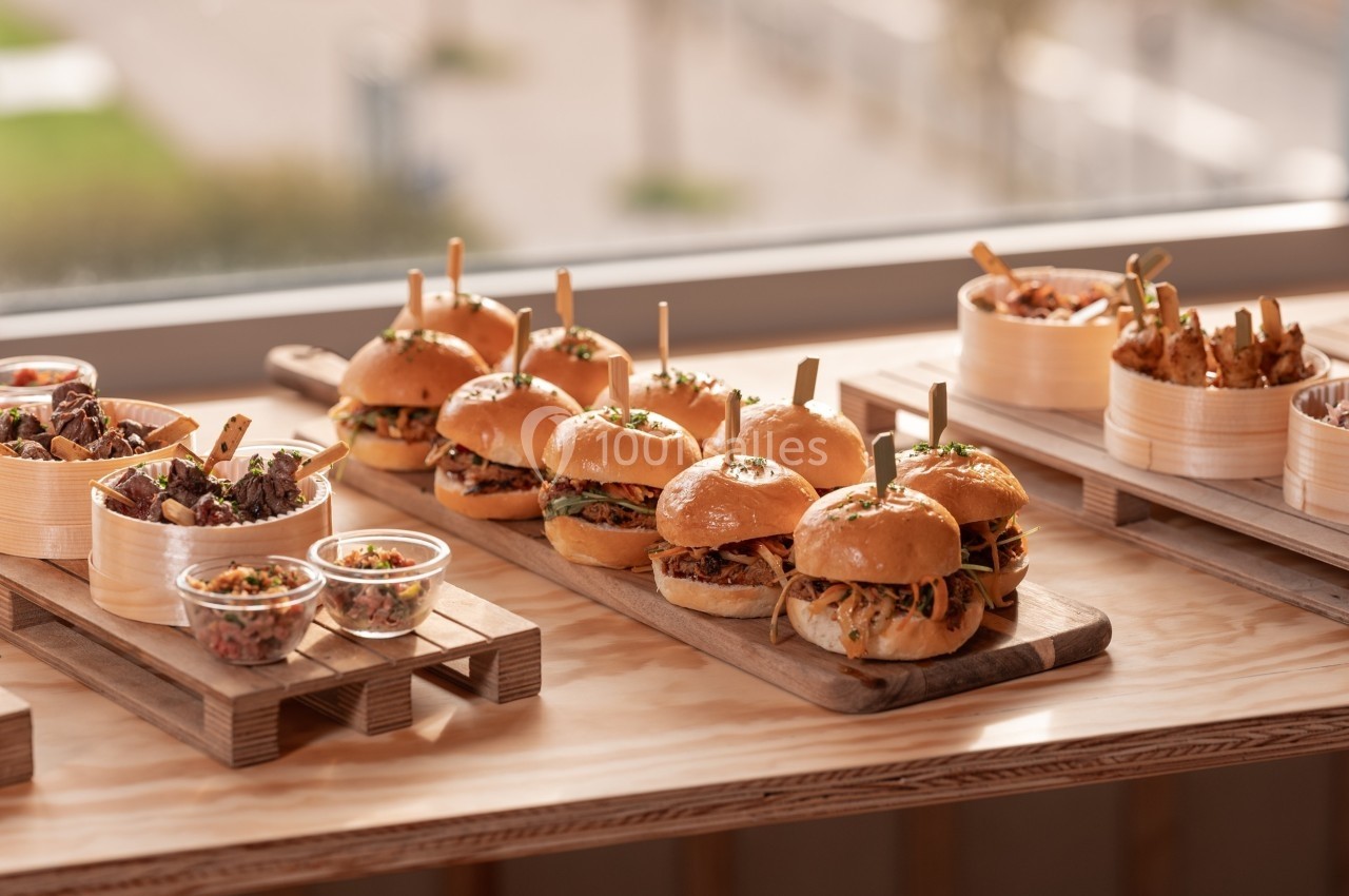 Plateau en bois avec burgers garnis, accompagnés de salades et de frites dans des contenants en bois.