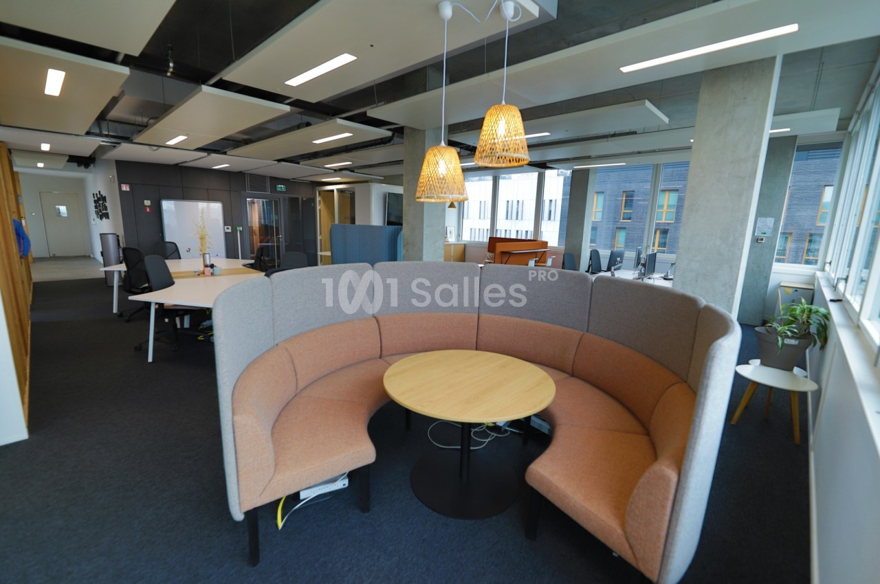 Espace de travail moderne avec mobilier en bois, canapé arrondi, lampes suspendues et grandes fenêtres.