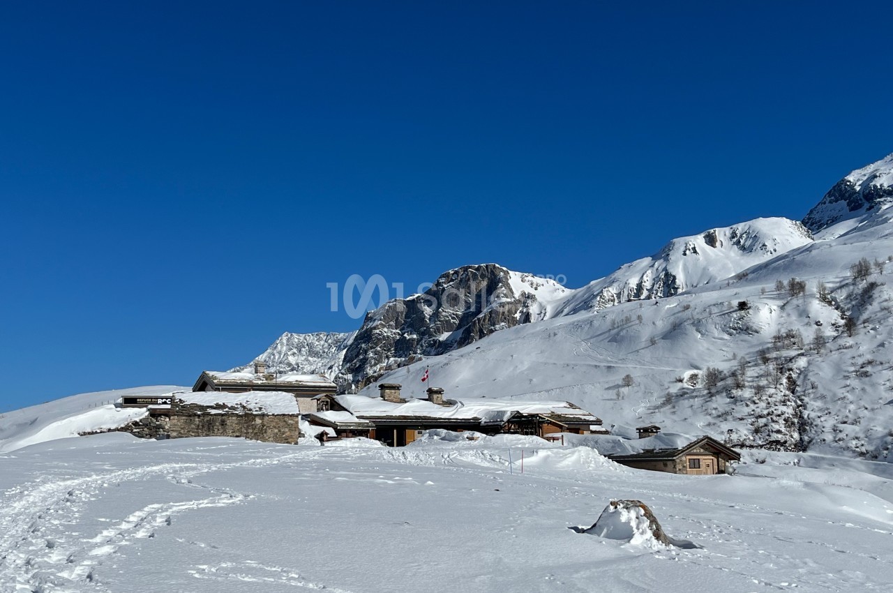 Chalets en bois entourés de neige au pied de montagnes sous un ciel bleu clair.