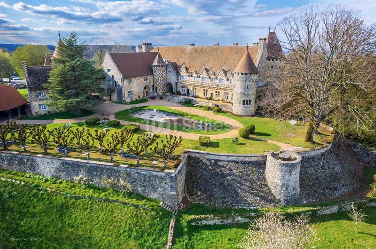Vue aérienne d'un château historique entouré de jardins, d'arbres taillés et de murs en pierre.