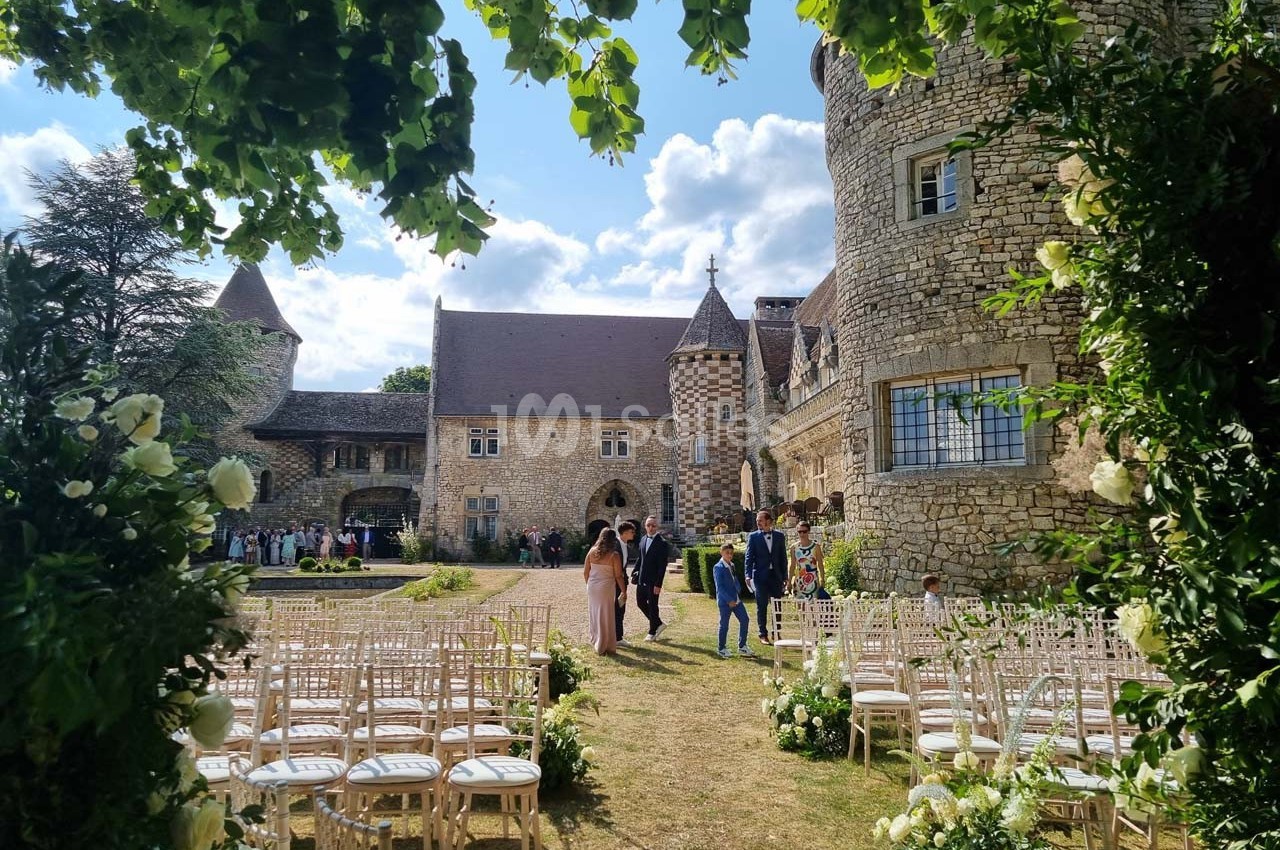 Cérémonie en plein air dans la cour d'un château en pierre, avec des chaises alignées et des invités en arrière-plan.