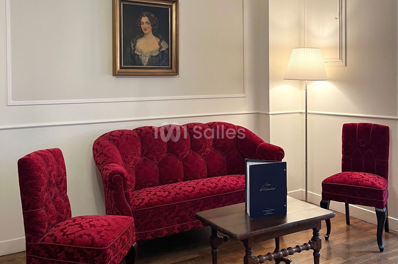 Salon avec canapé et chaises en velours rouge, table basse en bois, lampe sur pied et tableau au mur.