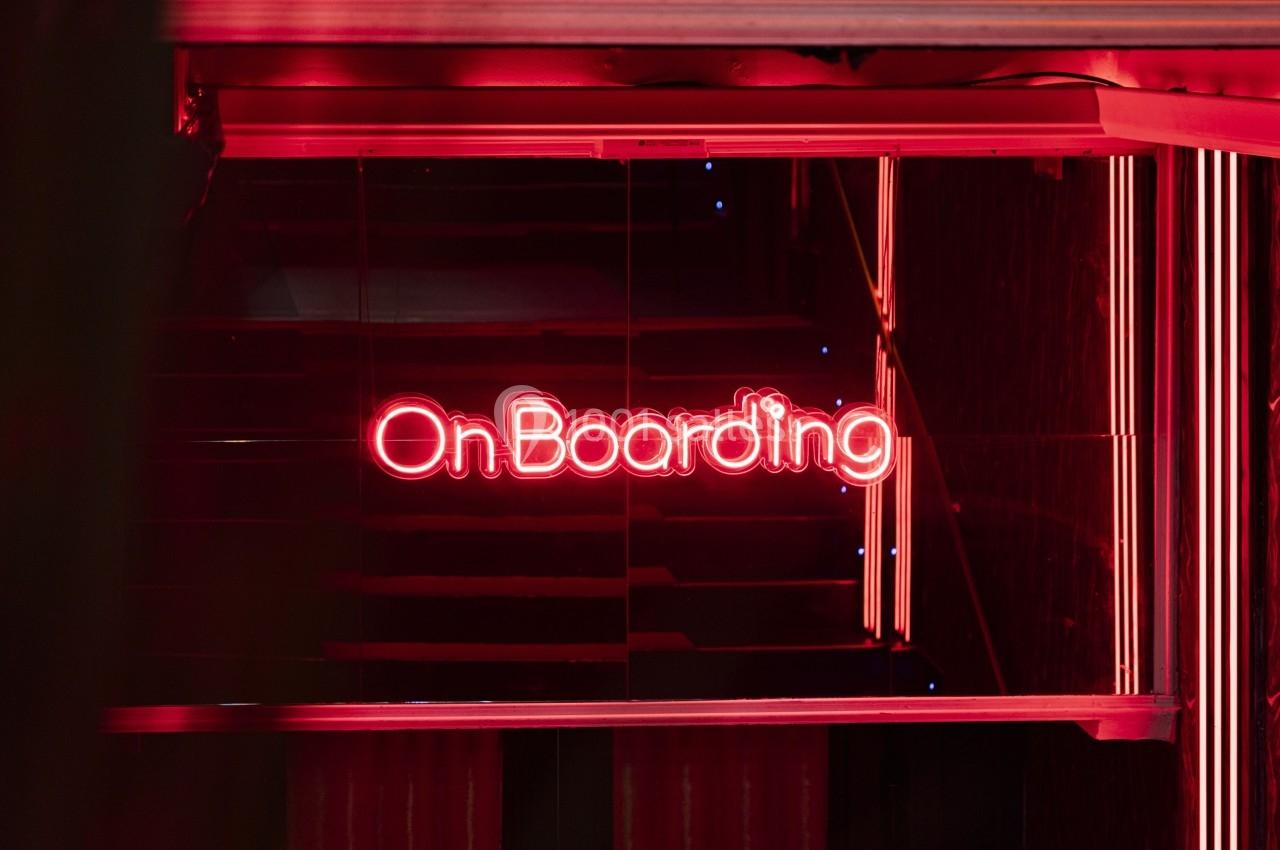 Enseigne lumineuse rouge affichant le mot ’OnBoarding’ dans un environnement sombre et moderne.