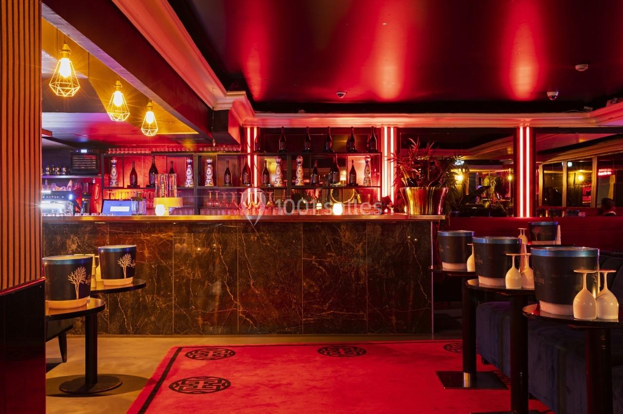 Bar élégant avec comptoir en marbre sombre, éclairage rouge tamisé et tables décorées de seaux à champagne.