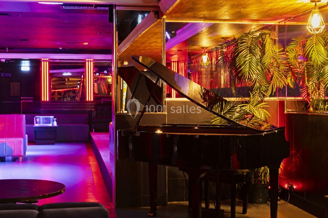 Piano à queue noir dans un intérieur de bar ou lounge avec éclairage tamisé et plantes décoratives.