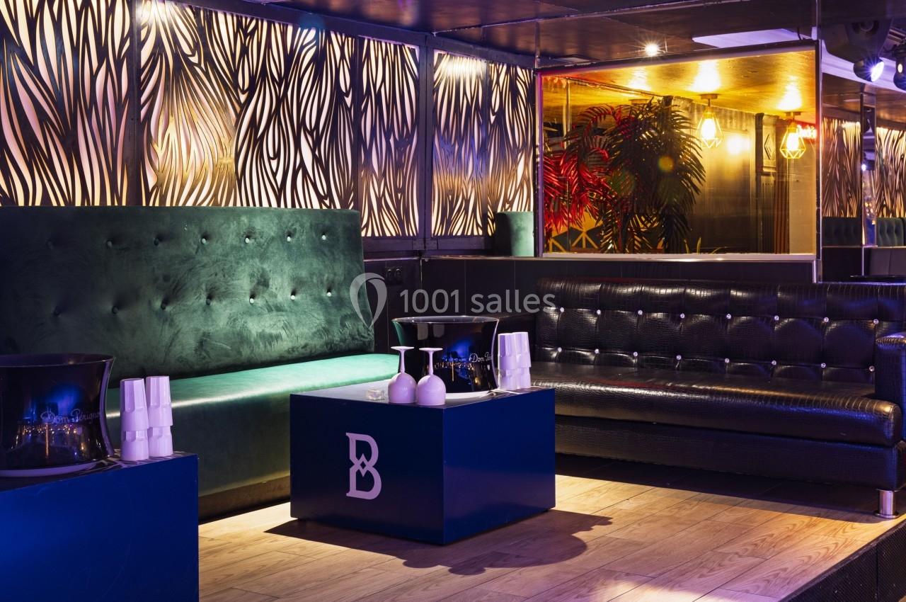 Deux canapés, un vert et un noir, entourent une table basse bleue dans un intérieur lumineux et décoré.