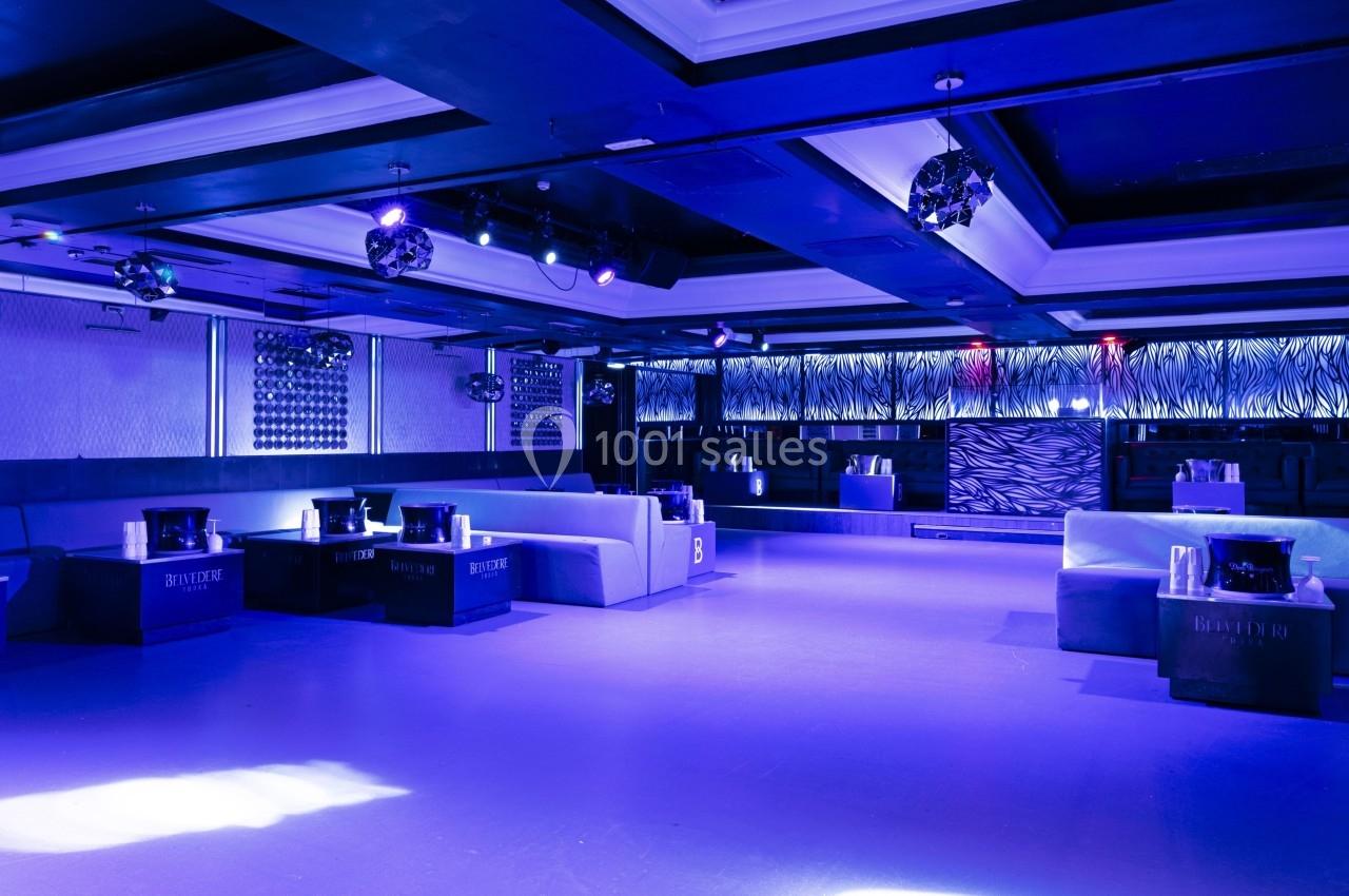 Salle de club nocturne avec éclairage bleu, banquettes, tables basses et décorations modernes.