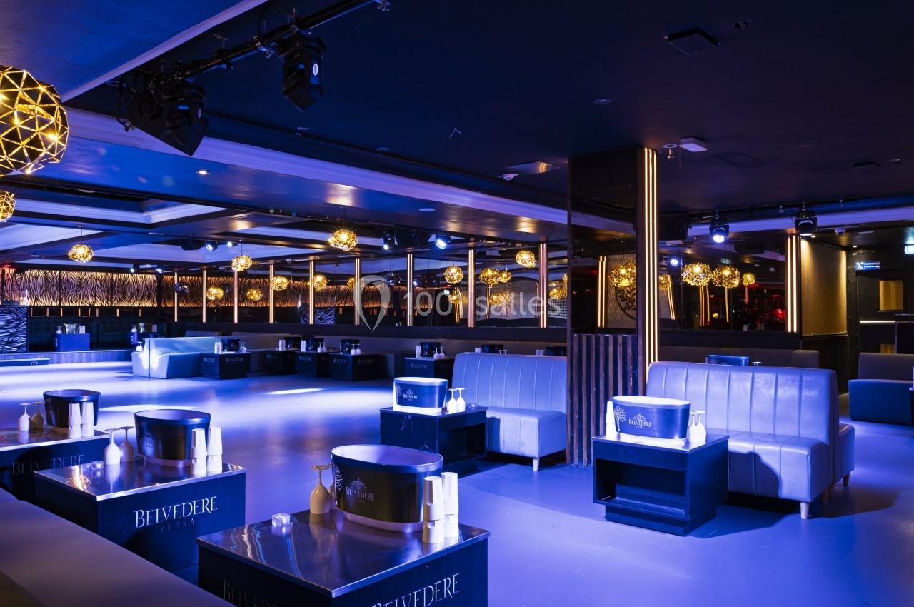 Salle de club moderne avec éclairage tamisé, banquettes en cuir et tables basses noires.