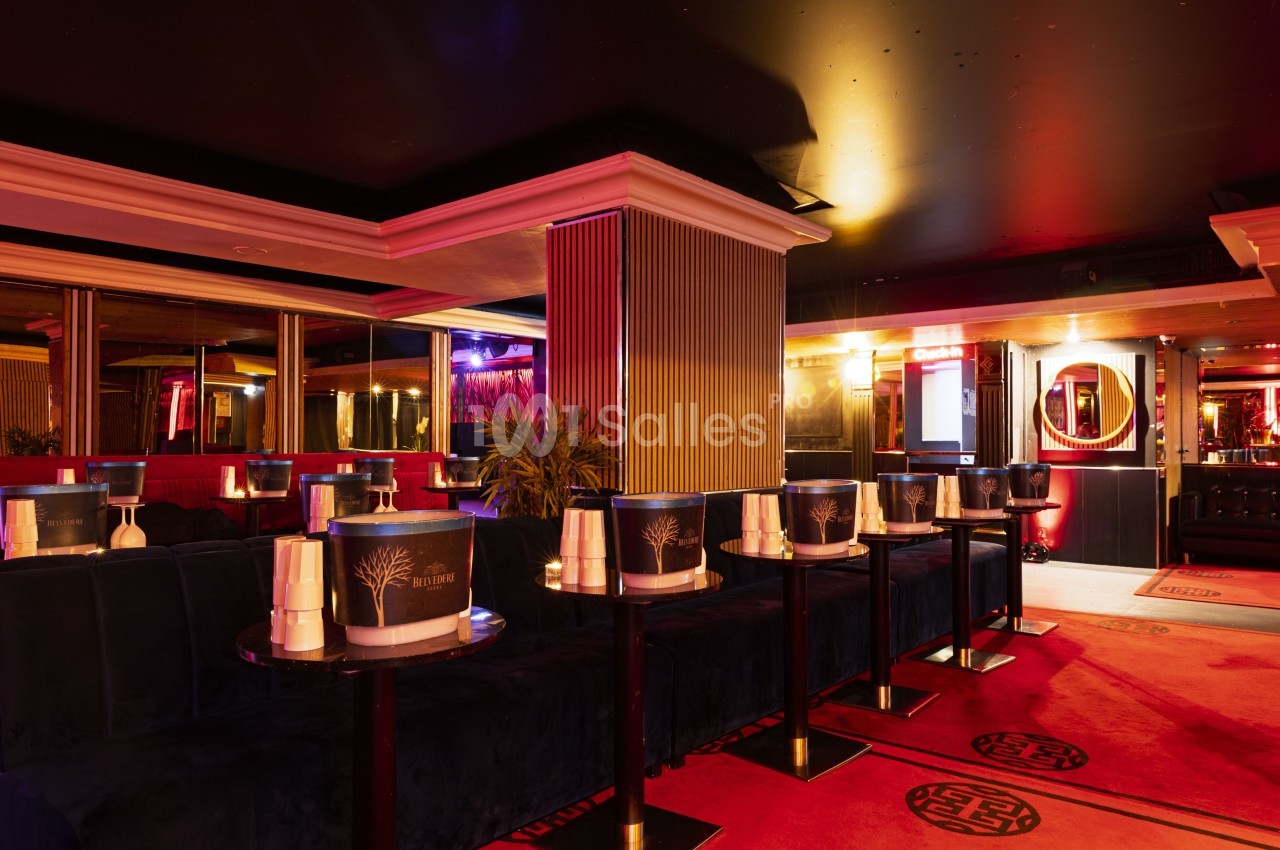 Salle de réception élégante avec banquettes rouges, tables basses noires et éclairage tamisé dans une ambiance nocturne.