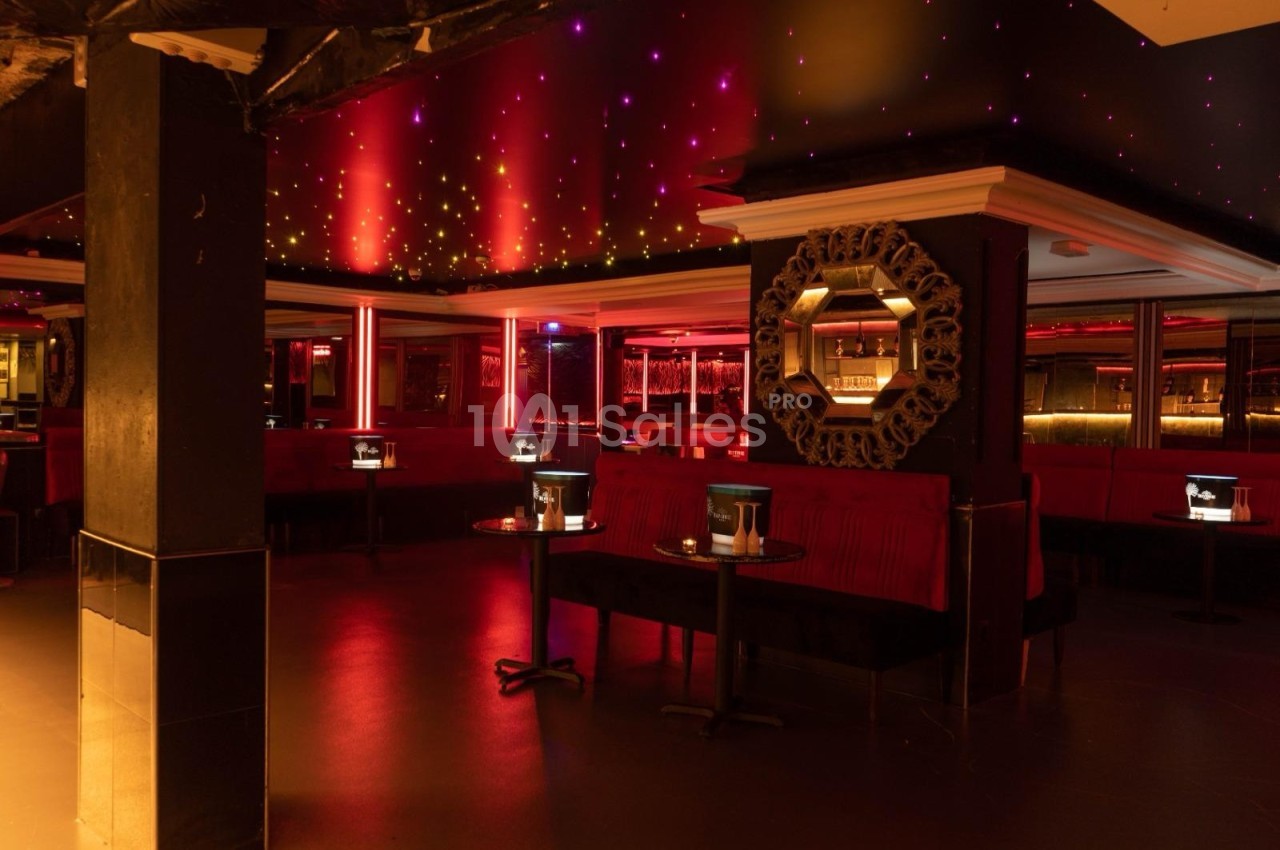 Salle de bar avec banquettes rouges, tables basses éclairées et plafond étoilé dans une ambiance tamisée.