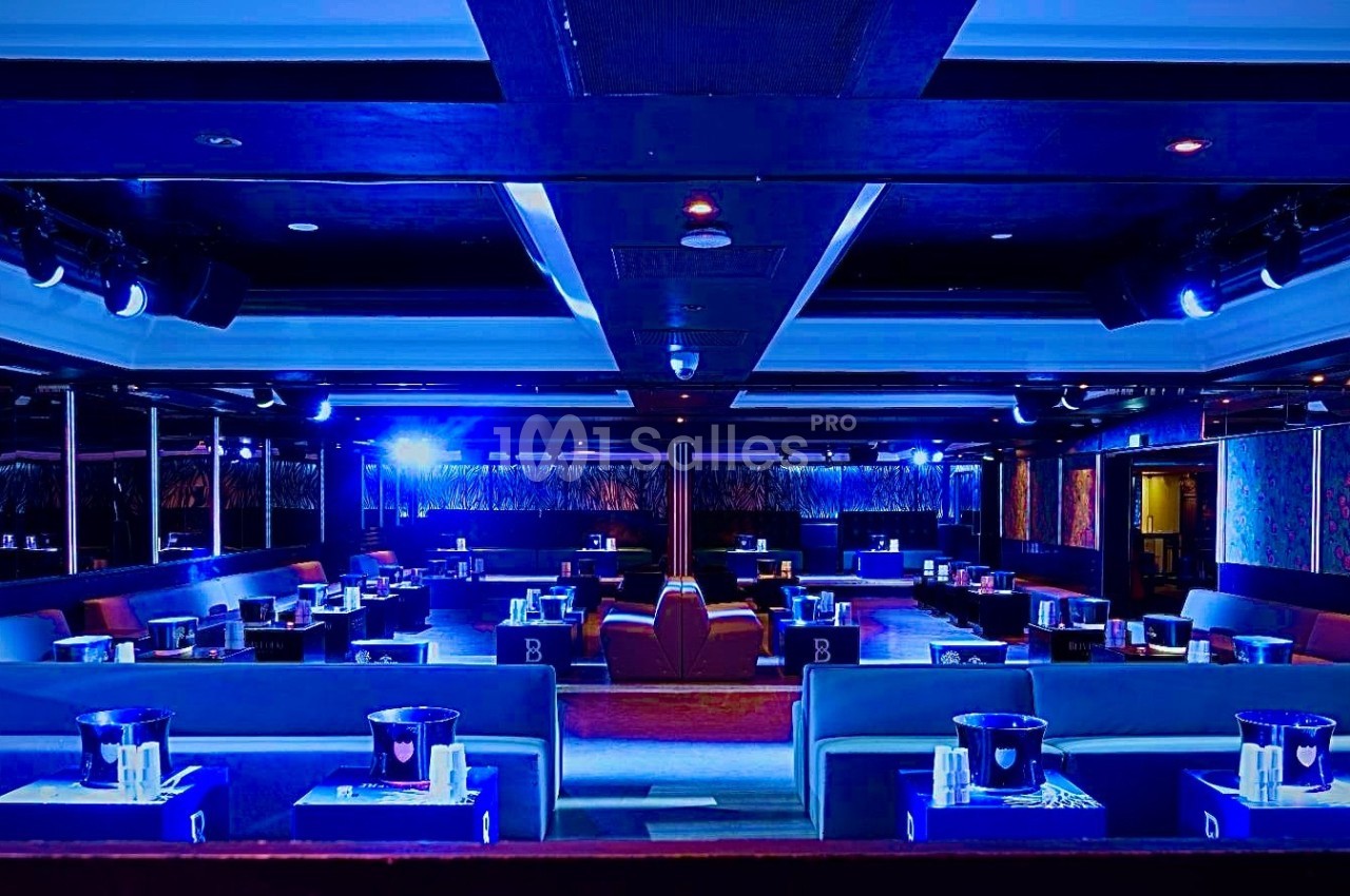 Salle de réception moderne avec éclairage bleu, tables dressées et banquettes alignées dans un cadre élégant.