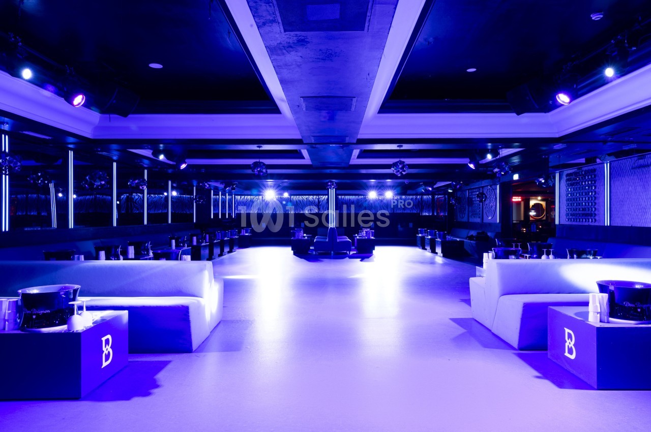 Salle de réception moderne avec éclairage violet, canapés blancs et tables basses disposées symétriquement.