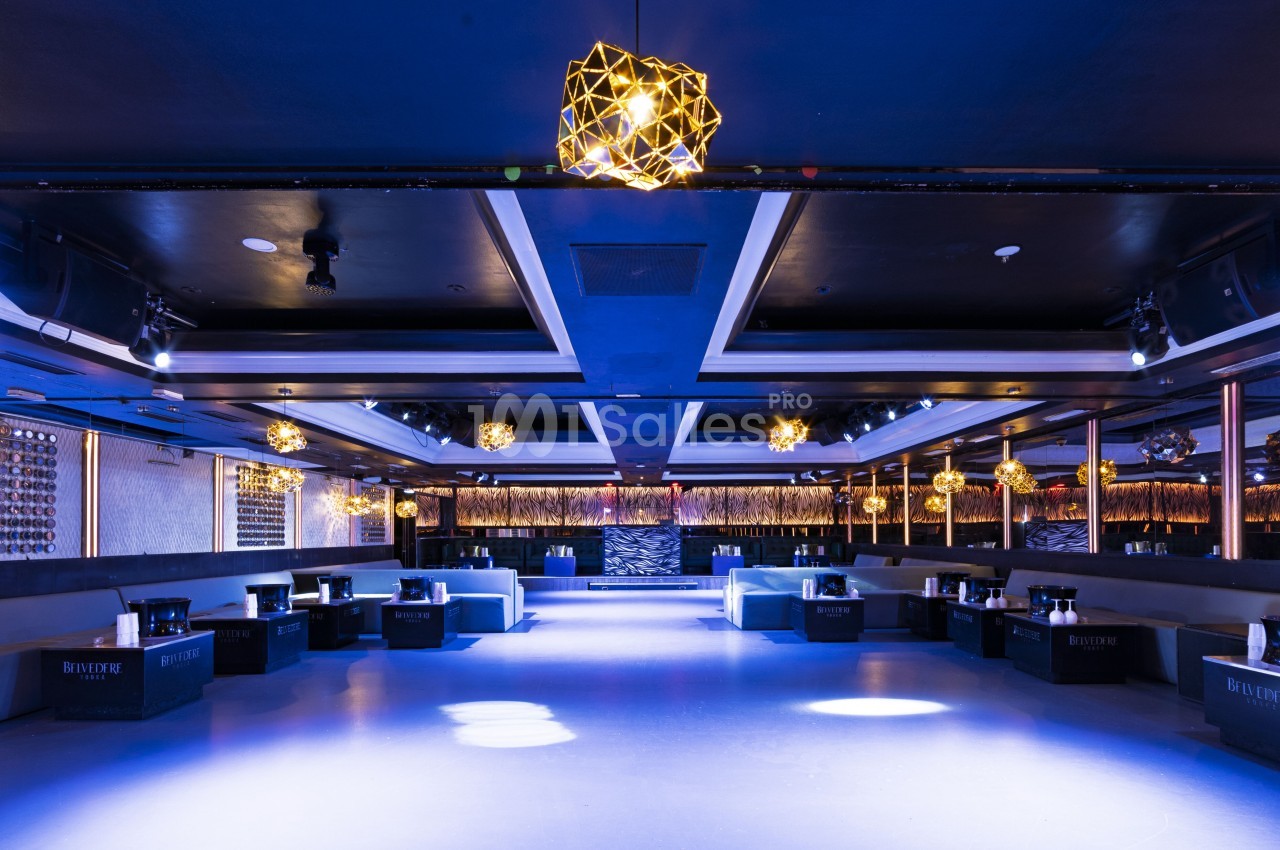 Salle de réception moderne avec éclairage tamisé, canapés alignés et décorations lumineuses suspendues.