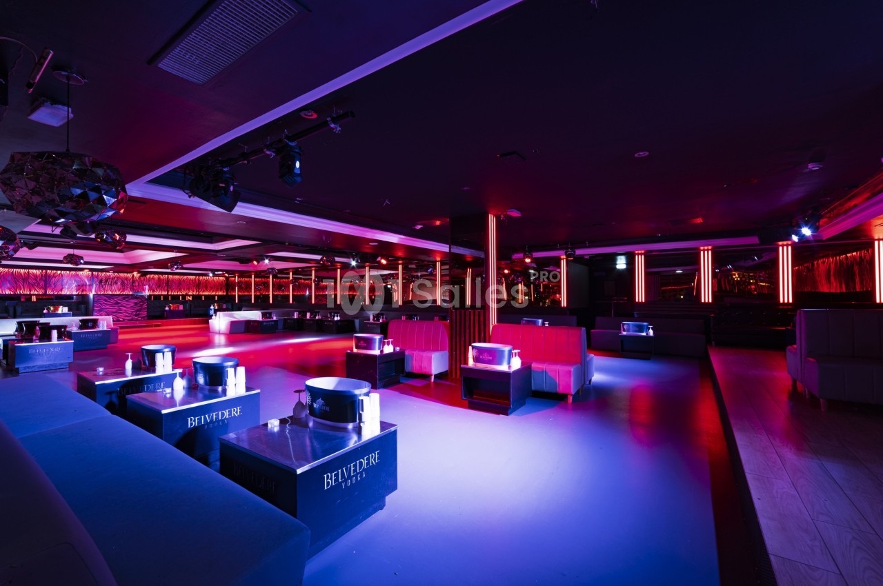 Salle de discothèque avec éclairage tamisé, banquettes rouges, tables basses et piste de danse centrale.