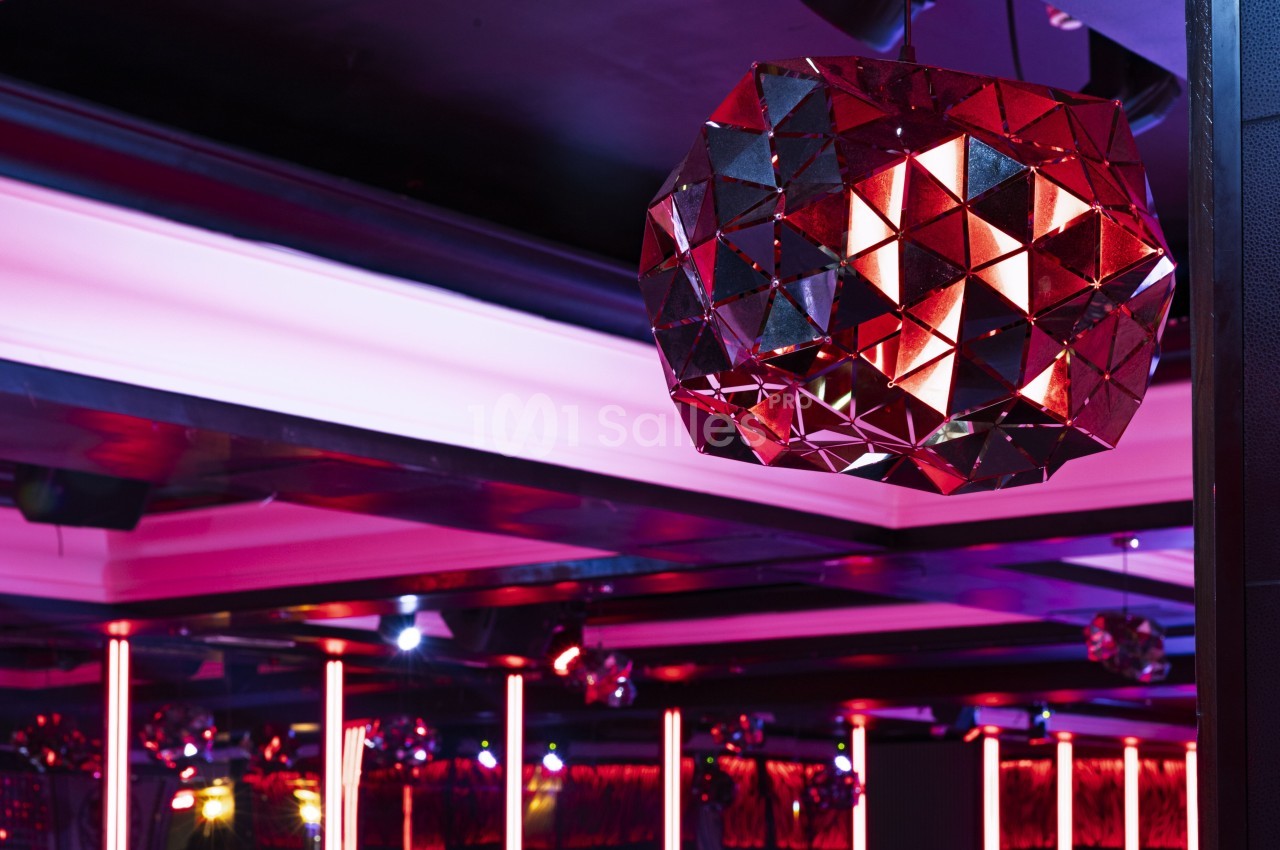 Lustre géométrique rouge suspendu dans un intérieur moderne avec éclairage néon et plafond sombre.